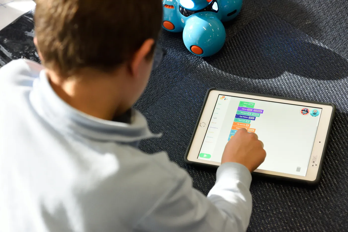 Ein Kind programmiert auf einem iPad mit farbigen Blöcken einen kleinen Roboter